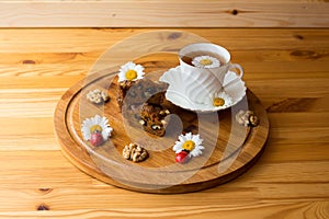 Carrot cakes cut with walnuts and spices,a white porcelain Cup with a saucer and tea, walnuts, daisies with ladybirds. All on a