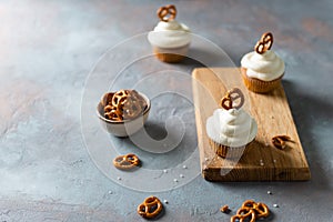 Carrot cupcakes with cream cheese and brezel on wooden board on dark background. Bakery, confectionery, party
