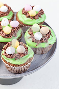 Carrot cupcakes with cream cheese frosting and Easter chocolate eggs, on gray cake stand, vertical