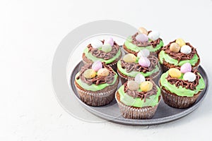Carrot cupcakes with cream cheese frosting and Easter chocolate eggs, on gray plate, horizontal, copy space