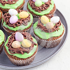 Carrot cupcakes with cream cheese frosting and Easter chocolate eggs, on gray plate, square format