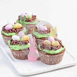 Carrot cupcakes with cream cheese frosting and Easter chocolate eggs, on white plate, square format