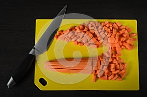 Carrot cut with knife for cooking on a yellow cutting board on a dark background