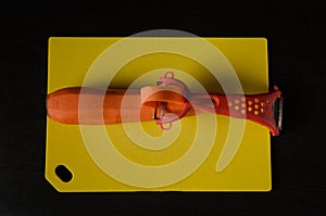 Carrot cut with knife for cooking on a yellow cutting board on a dark background