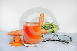 Carrot juice in a glass cup, glasses for vision on a light gray concrete background. Concept carrot for good eyesight