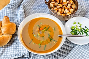 Carrot soup in plate, bread, onion shoot and piece of fried bread in bowl