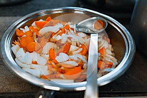 Carrots and onions are stewed in a large shiny plate on the stove. Vegetables are prepared for eating