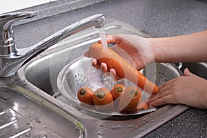 Carrots are washed under running water in a colander