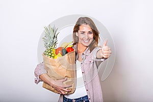 Carrying a healthy bag. Cropped image of beautiful young woman in apron holding paper shopping bag full of fresh vegetables and