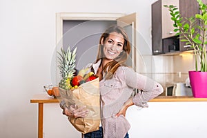 Carrying a healthy bag. Cropped image of young woman in apron holding paper shopping bag full of fresh vegetables and