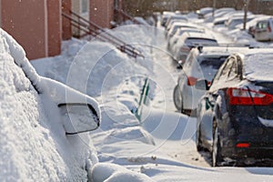 cars buried under snow in parking near residental building at sunny day light