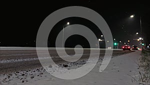 Cars drive along a winter night street in the city. Roadway is covered with snow. Danger of slipping and occurrence of a