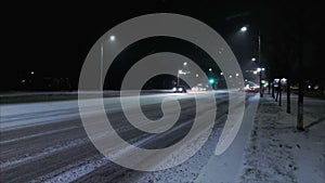 Cars drive along a winter night street in the city. Roadway is covered with snow. Danger of slipping and occurrence of a