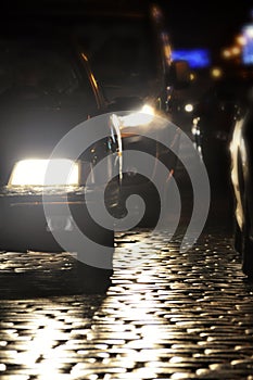 Cars drive on a cobblestone street at night, car lights on the street headlight