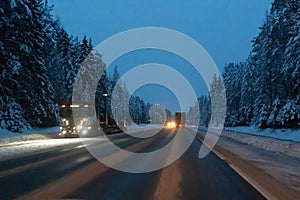 Cars drive with headlights on the winter road in a snow storm in the twilight when snow is flying. Concept of driving in