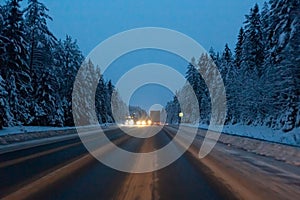 Cars drive with headlights on the winter road in a snow storm in the twilight when snow is flying. Concept of driving in