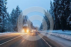 Cars drive with headlights on the winter road in a snow storm in the twilight when snow is flying. Concept of driving in