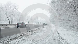 cars driving along snowy winter road divided with concrete barrier surrounded with frost covered trees