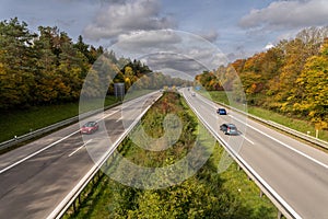 Cars are driving fast over a highway at the fall time, framed by beautiful trees, centred view.