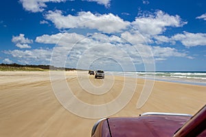 Cars driving on the main transportation highway on Fraser Island - wide wet sand beach coast facing Pacific ocean - long 75 miles