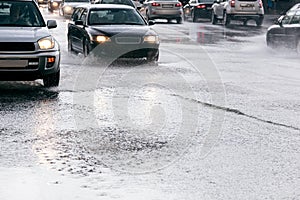 Cars driving on road with water puddles during heavy rain