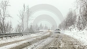 Cars driving on snow covered forest road during snowstorm, fog in disance, view from car behind. Dangerous driving conditions