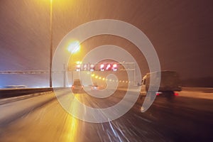 Cars fast drive on the winter speedway or highway with roadway lighting in a snow storm in the twilight when snow with