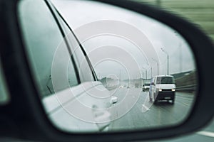 Cars on the highway in the rain in the side mirror. Close-up