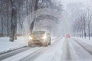 Cars moving on slippery snowy road at city street during heavy snowfall at evening in winter . Traffic obstacle due blizzard and