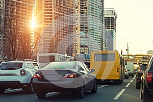 Cars onhighway at city traffic jam with sunset sun lights through hightower construction site on background. Metropolis evening