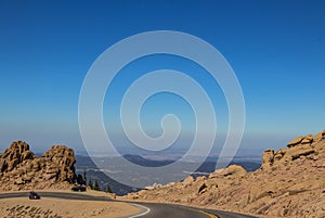 Cars parked on edge of curved mountain road above the tree line on Pikes Peak Colorado with people climbing bare boulders and pano photo