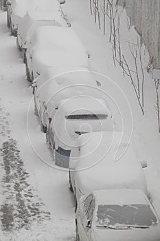 Cars parked near the house covered with snow. Vertical photo. Snowy winter in the city