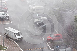 Cars parked at a parking lots near high-rise building under heavy shower rain and hurricane wind