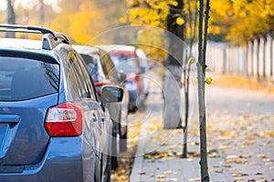 Cars parked in a row on a city street side on bright autumn day