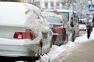 Cars parked on a side of city street covered with dirty snow in winter