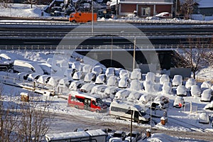 Cars on parking and street covered with big snow layer. View of winter and snowing on city street with snowflakes.