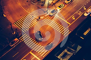 Cars and people on road intersection with signal lights and crosswalks at night time in the city street.