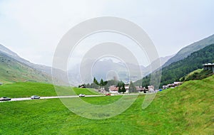 Cars riding trough mountain road in Swiss alps and small village on horizon.