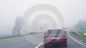 Cars on the road in the fog. Bad weather and dangerous automobile traffic on the road. Light vehicles in fog. Foggy gray