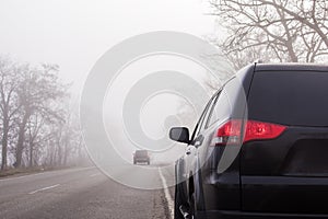 Cars on the road in the fog. Bad winter weather and dangerous automobile traffic on the road. Light vehicles in fog. Foggy gray