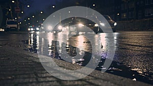 Cars slowly passing streets on rainy night, water on the road reflecting light