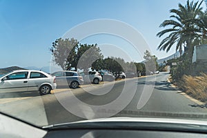 cars stopped on the edge of a road, driving in Agios Nikolaos, palm trees and lake view