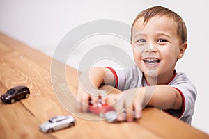 Cars, toys and boy kid by table playing for learning, development and fun at modern home. Cute, sweet and portrait of