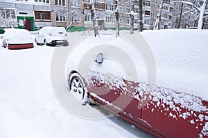 Cars under snow after heavy snowfall on winter town street in courtyard of apartment building