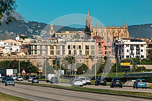 Cars on the urban road as residential buildings and famous cathedral on background in Palma, Spain