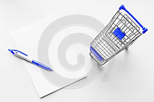 Cart from the grocery store and blank sheet of paper with pen on the white background. Shopping list. Business ideas.
