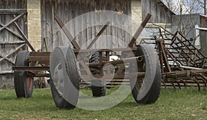 A horse-drawn cart on car wheels standing in front of a wooden barn.