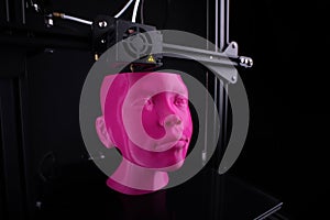 A cartesian 3D-printer manufactures a humanoid head from bright pink plastic.