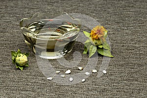 Carthamus tinctorius, American saffron, wild thistle. Safflower: bud, yellow flower, seeds and oil in a glass cup on a background photo