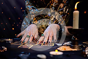 Cartomancy. A fortune teller reads Tarot cards. On the table are candles and fortune-telling objects and sparks. Hands close up. photo